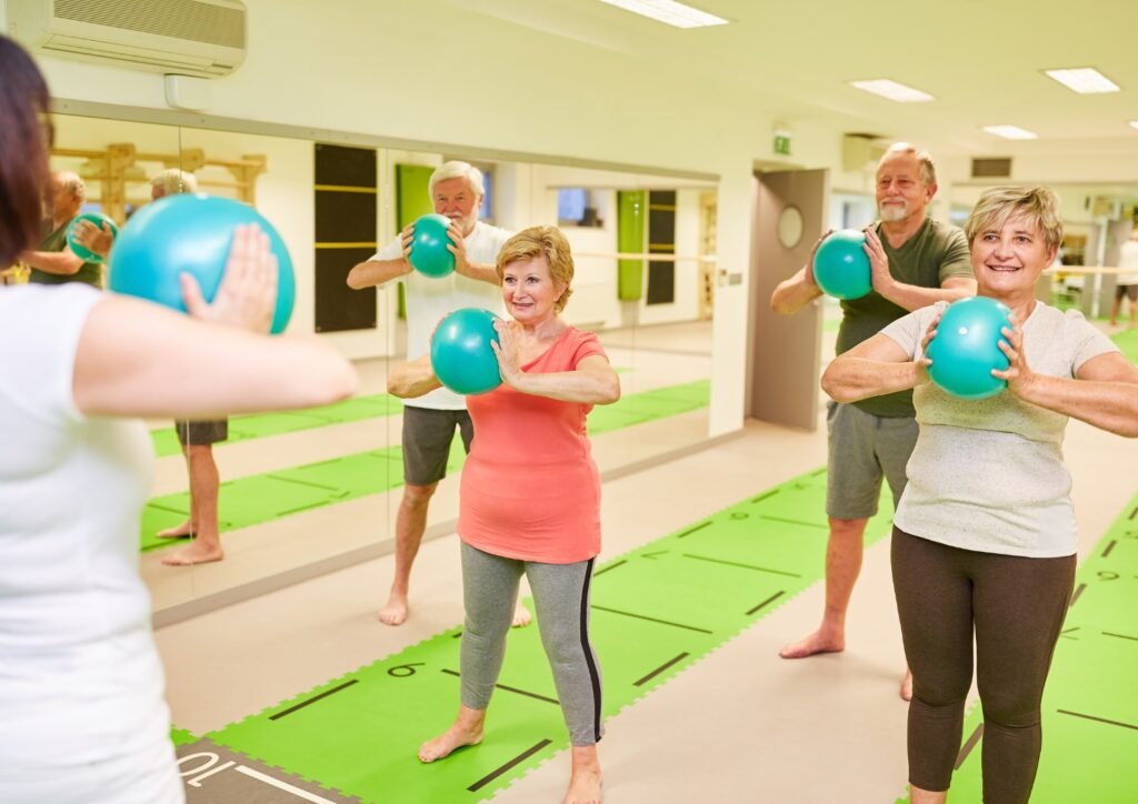 Seniors exercising with green medicine balls in a bright gym, participating in a group fitness class on green mats