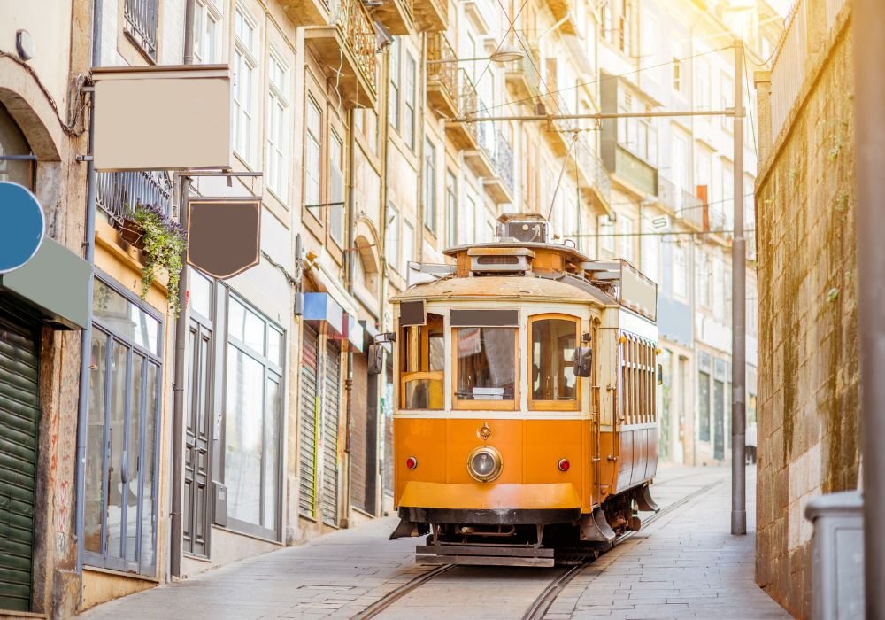 Historic orange tram travels through narrow cobblestone street lined with traditional Portuguese buildings in Porto