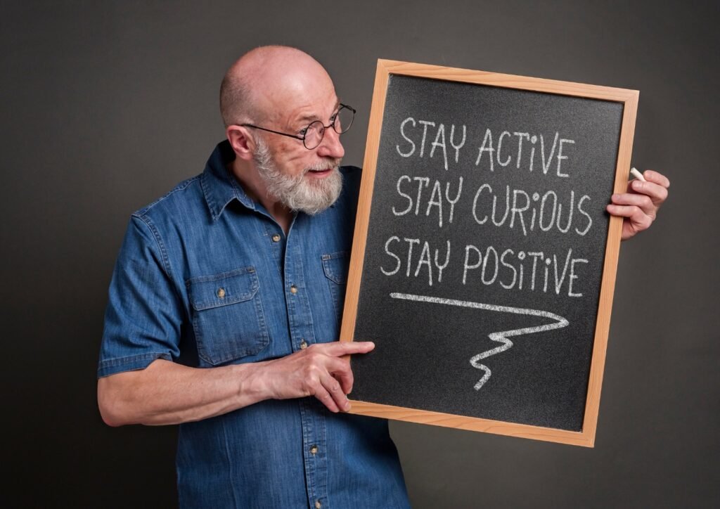 stay active, curious and positive - the keys to healthy aging, inspirational white chalk writing on a blackboard held by a senior man